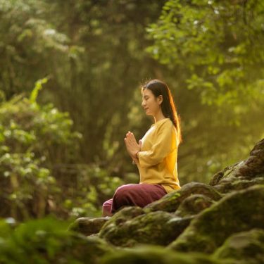 A woman meditates peacefully in a sunlit forest, embodying tranquility and connection with nature.