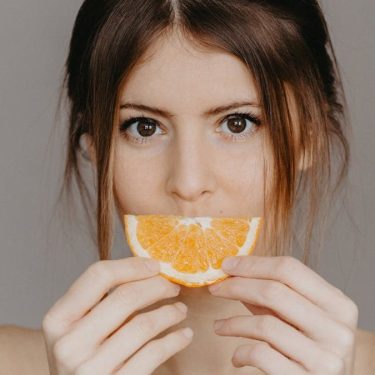 Close-up portrait of a woman holding a half orange slice, with a focus on natural beauty and skincare.