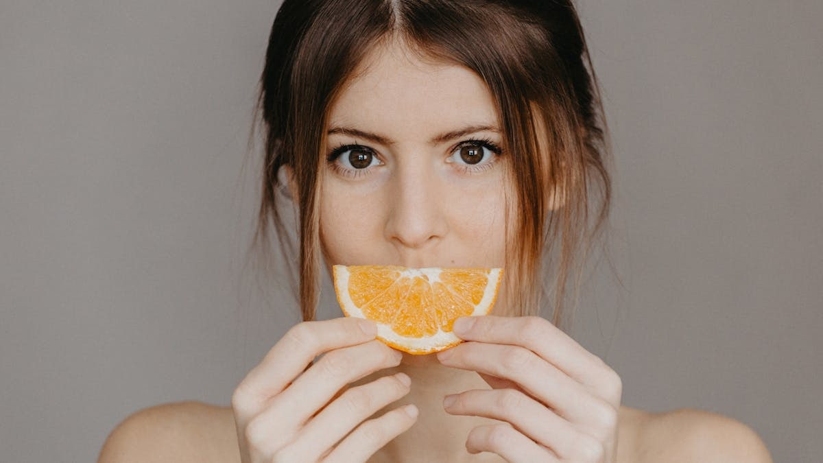 Close-up portrait of a woman holding a half orange slice, with a focus on natural beauty and skincare.